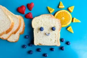

bread and fruit on a blue background. There is blueberries on the bread in the shape of a smiley face