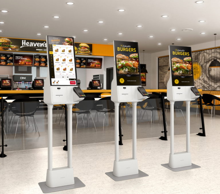 Three self service kiosks placed side-by-side inside a burger fast food restaurant.